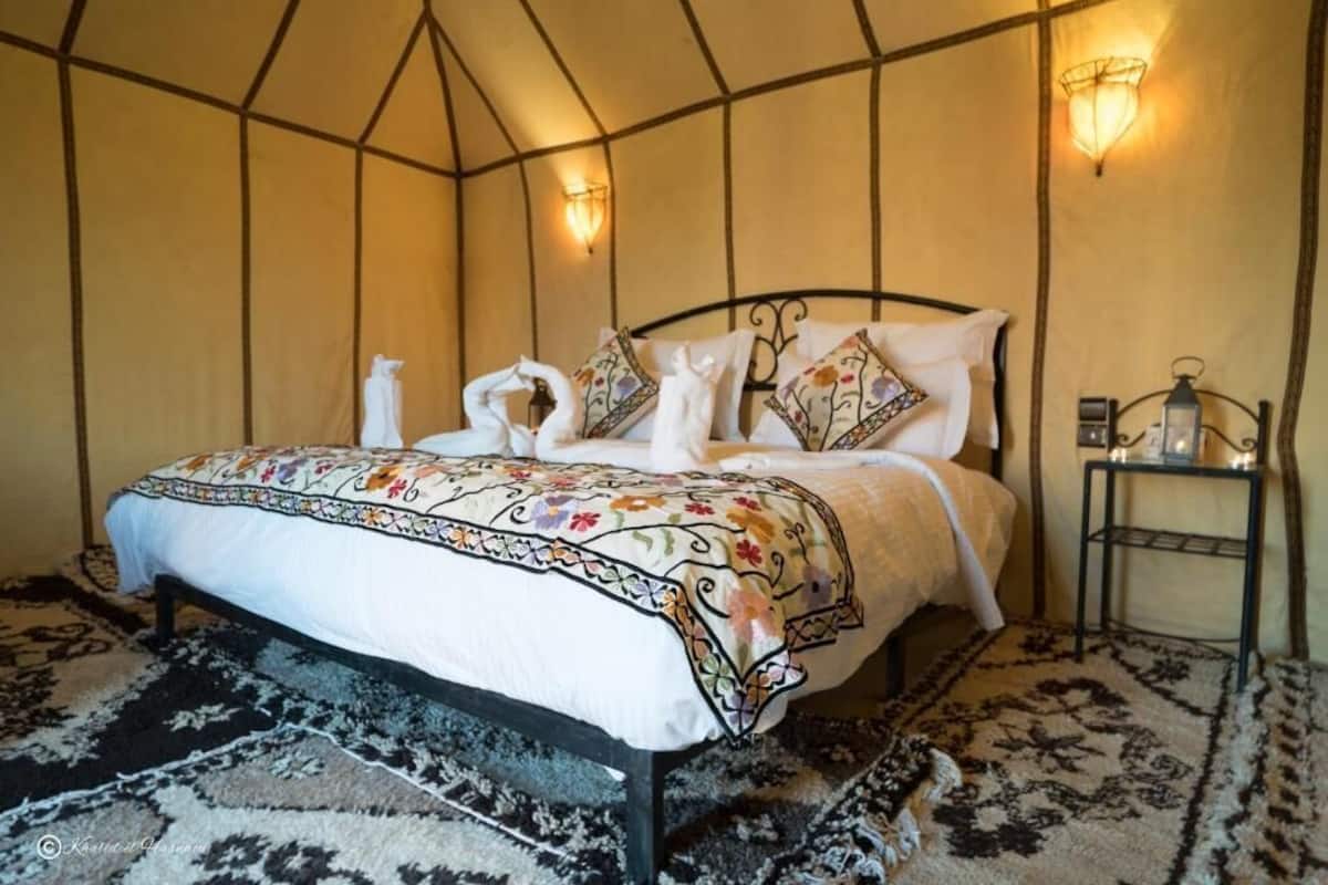 A room with a bed, a nightstand, and wall-mounted lights.