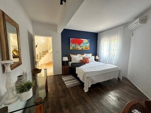 Quarto com cama, pintura, escada e janela com cortinas.