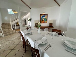 Uma sala de jantar com uma mesa posta para quatro pessoas, uma escada e um quadro na parede.