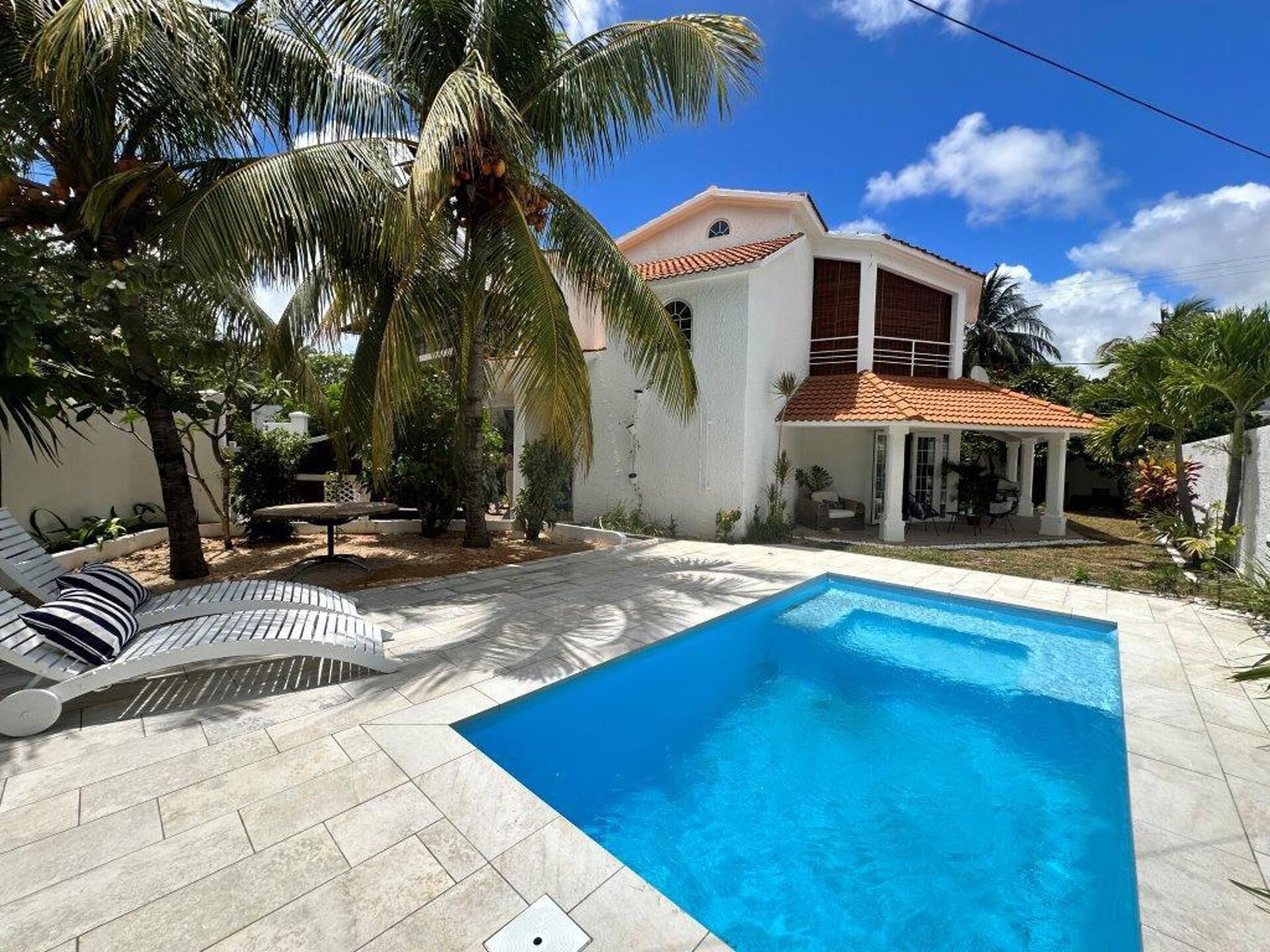 A swimming pool with a tiled deck, a lounge chair, and a palm tree.