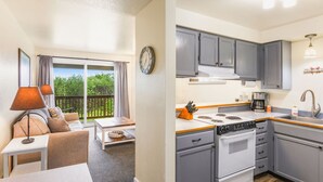 A compact kitchen with grey cabinets, a stove, and a sink. There's a dining area with a table and a sofa. - So Very Nice in Ocean Shores (Ocean Shores)