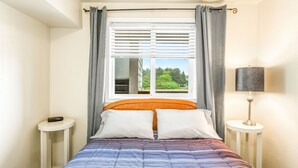 A bedroom with a bed, a window with curtains, a bedside table, and a lamp. - So Very Nice in Ocean Shores (Ocean Shores)