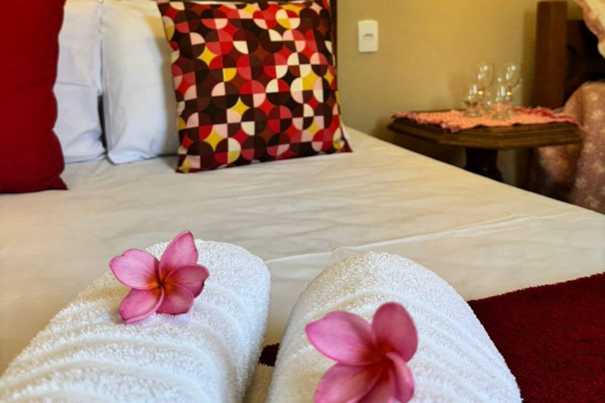 A hotel room with a bed, pillows, a table with glasses, and a lamp.