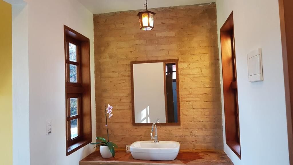 A bathroom with a white sink, a mirror, a wooden-framed window, and a hanging light fixture.