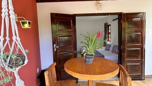 A wooden table with chairs, a macrame wall hanging, and a potted plant on a red wall. - Pousada Chalé Cantinho de Minas  (São João Batista do Glória)