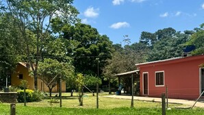 A fenced grassy area with a red building, trees, and a clear sky. - Pousada Chalé Cantinho de Minas  (São João Batista do Glória)