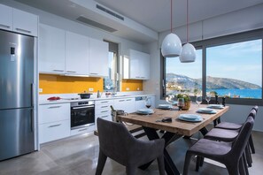 A modern kitchen with white cabinets, a stainless steel refrigerator, and a wooden dining table set for six with chairs.