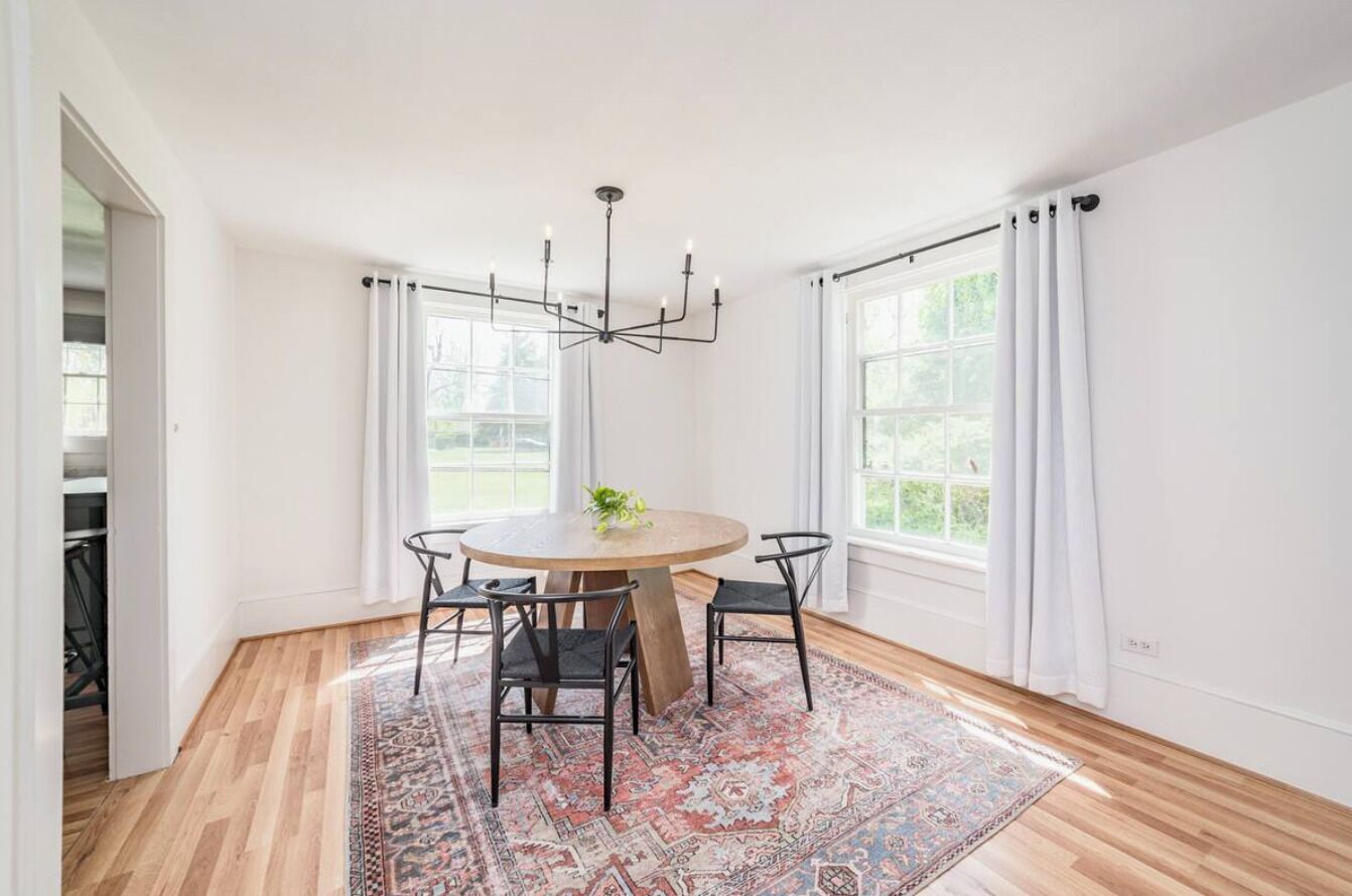 A dining area with a round table, four chairs, a chandelier, and a patterned rug.