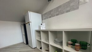 Une cuisine avec un réfrigérateur blanc, une étagère intégrée où sont rangées des assiettes et des tasses vertes, et un sol à motifs en chevrons.