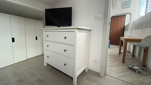 Une pièce moderne et bien éclairée, avec une commode blanche, un téléviseur à écran plat et un coin repas comprenant une table et des chaises.