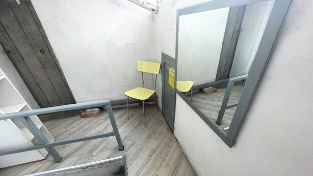 Un couloir étroit avec un plancher en bois, une rambarde en métal et une chaise jaune.
