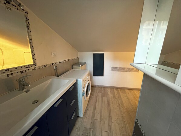A modern bathroom with a sink, mirror, and washing machine. - A Roof in the City (Genova)