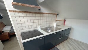 Une cuisine de taille réduite, dotée d’une cuisinière intégrée, d’un évier et de meubles de rangement de couleur sombre.