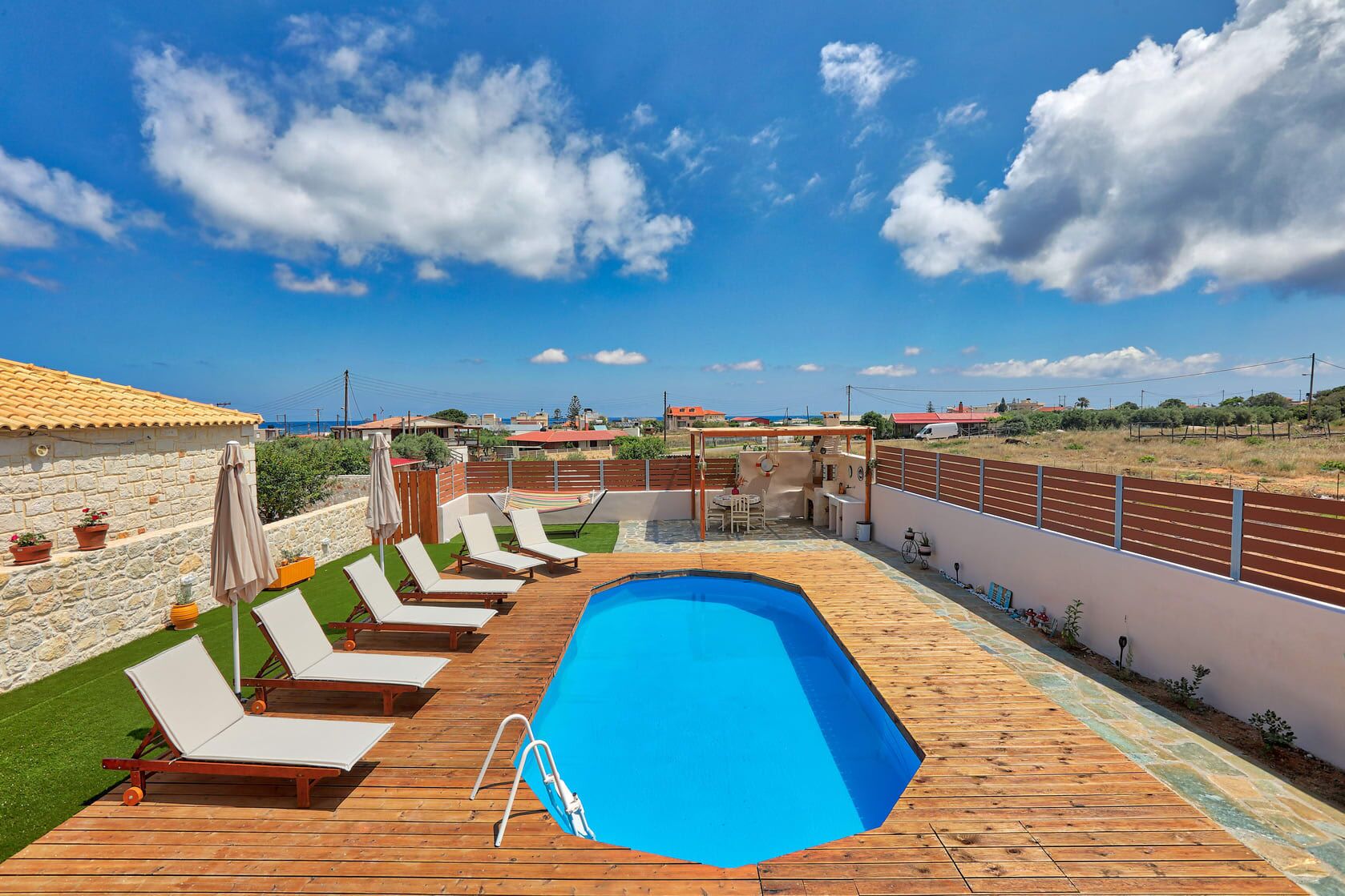 A swimming pool with lounge chairs, a wooden deck, and a stone wall.