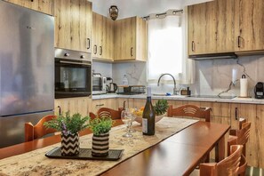 A kitchen with wooden cabinets, stainless steel appliances, a dining table with chairs, and a window with curtains.