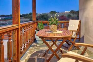 A wooden deck with a round table and two chairs, a potted plant, and a view of the landscape. - Anacosta Villa w/ Private Pool, Cretan Seaside Gem (Anisaras, Hersonisos)