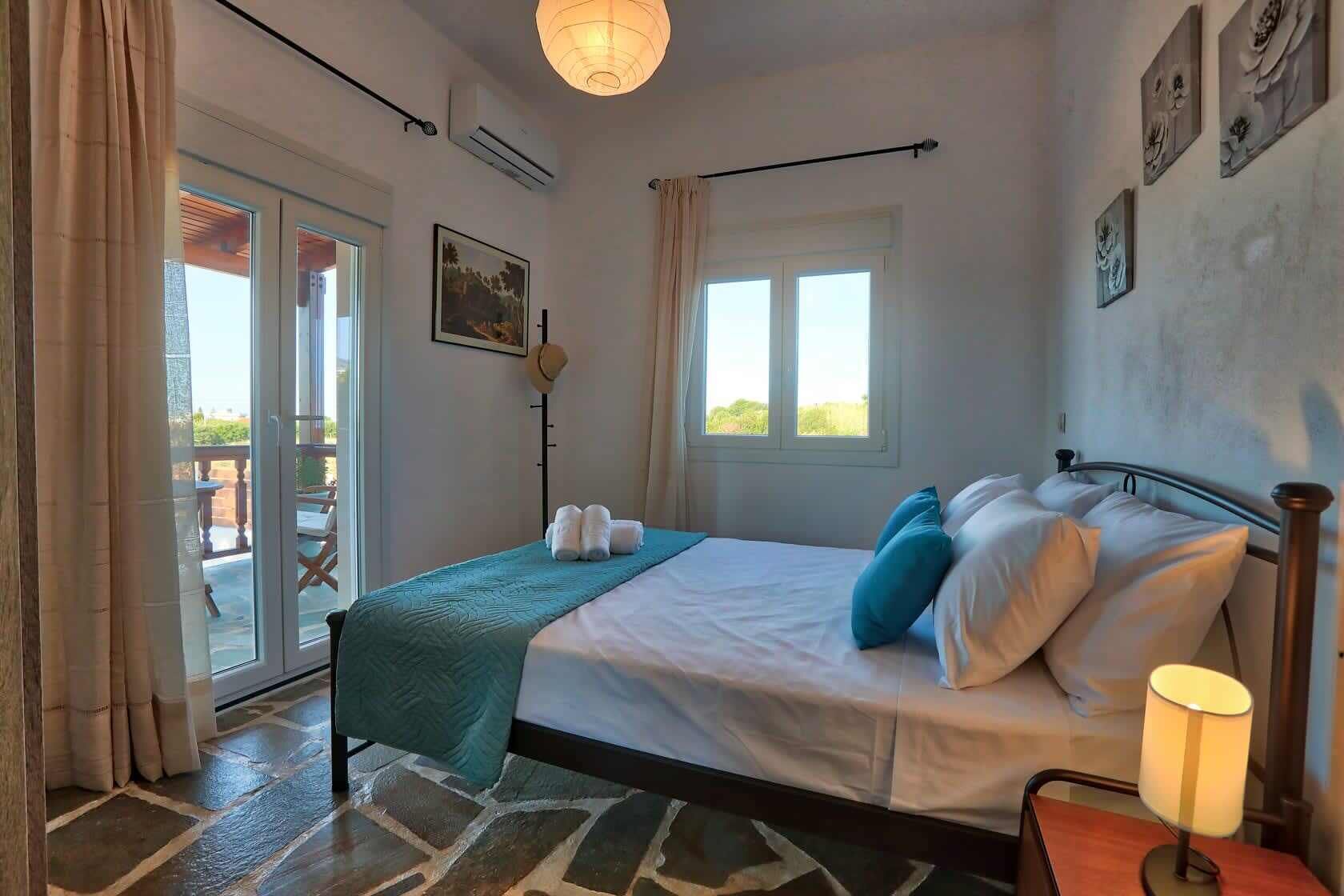 Un dormitorio con cama, mesita de noche, lámpara, ventana y puerta que da a un espacio exterior.