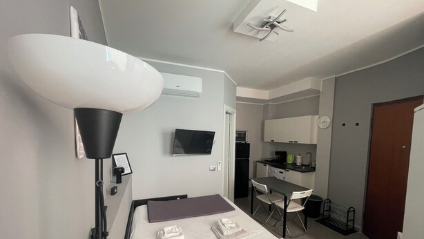 A compact hotel room with a bed, bedside lamp, TV, kitchenette, and a small dining area. - Pretty Flat Alassio Moglio (Moglio)