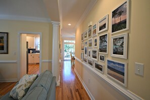 A hallway with a wooden floor, a light blue sofa with floral cushions, and a wall adorned with framed pictures. - Cock Tales- with Community Pool North Litchfield (Pawleys Island)