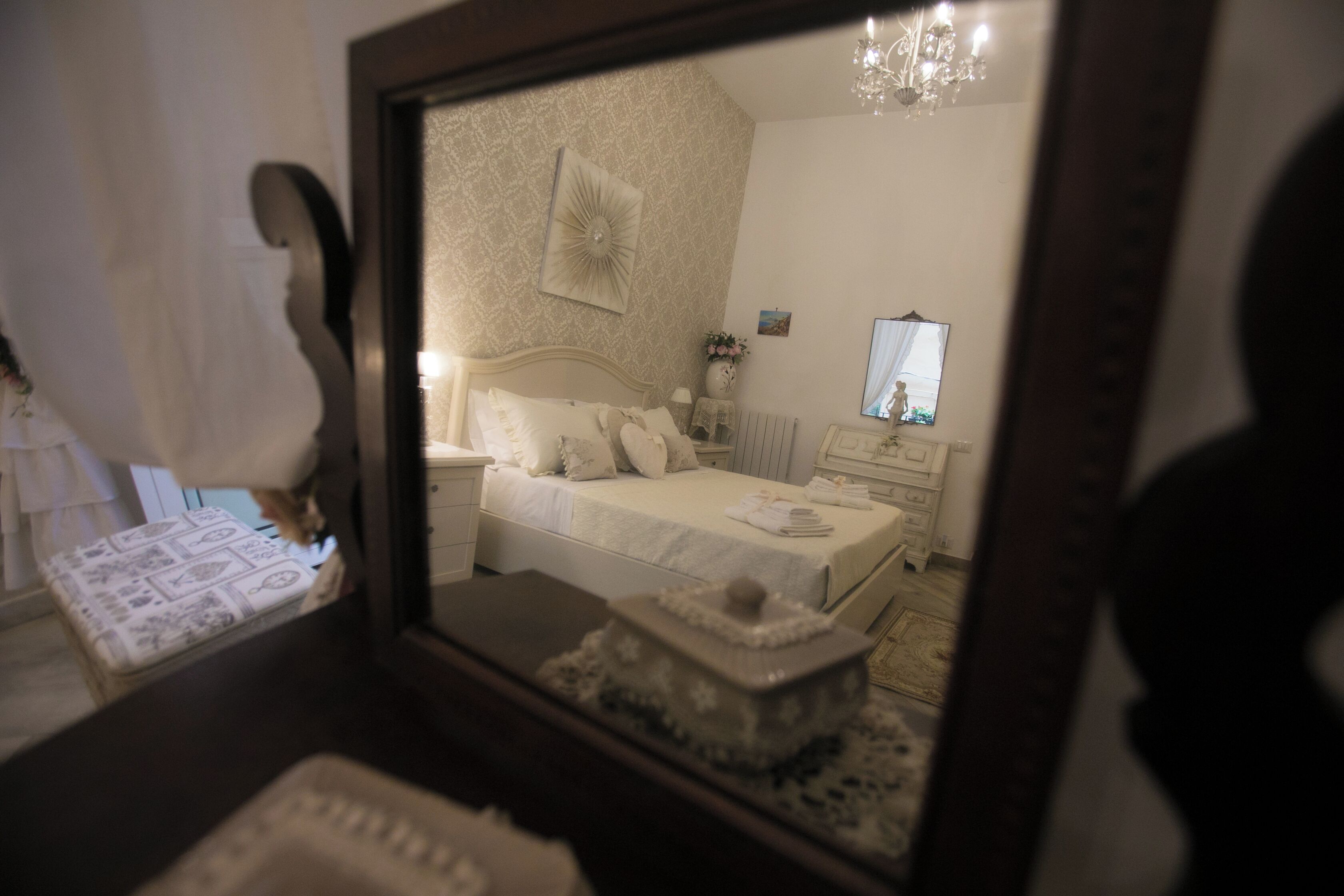 A bedroom with a bed, bedside table, lamp, and a mirror reflecting the room.