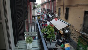 A narrow street with buildings on either side, a small outdoor seating area with tables and chairs, and a few people walking.