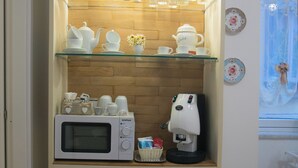 A kitchenette with a microwave, coffee maker, and glass shelves holding tea sets and cups.
