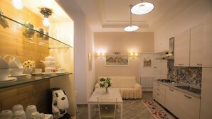 A modern kitchen with white cabinets, a dining table with chairs, a coffee machine, and a floral rug.