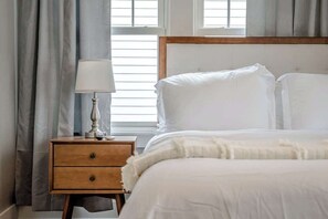 A bedroom with a bed, a nightstand with a lamp, and a window with curtains.