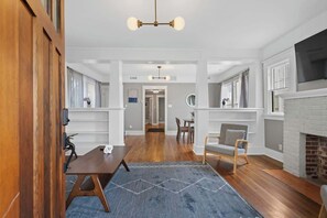 A spacious living room with a fireplace, wooden flooring, and a blue rug.