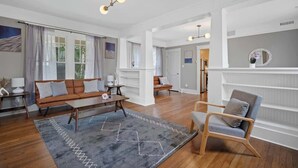 Amplia sala de estar con sofá, sillón, mesa de centro, piso de madera y un ventanal con cortinas.