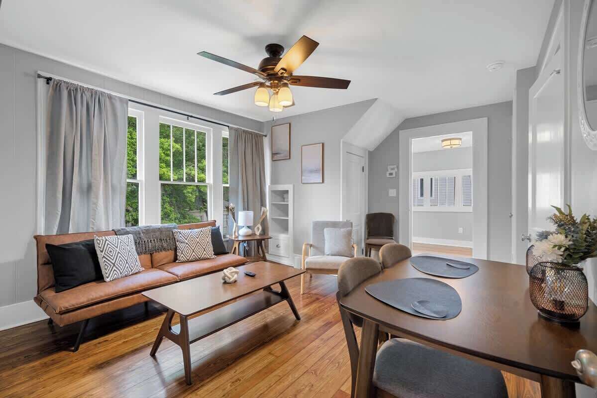 A modern living room with a sofa, coffee table, dining table, and ceiling fan.