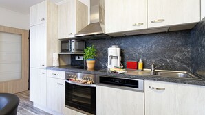 A modern kitchen with light wood cabinets, stainless steel appliances, a marble backsplash, and a built-in oven.