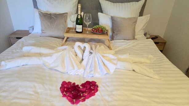 A neatly made bed with towels arranged in a heart shape, a bottle of champagne, and a plate of strawberries on a tray. - Moderne Ferienwohnung Sauerland am Bikerpark (Winterberg)