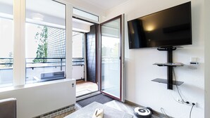 A modern room with a large TV mounted on the wall, a sliding glass door leading to an outdoor area, and a small table with a remote control. - Moderne Ferienwohnung Sauerland am Bikerpark (Winterberg)