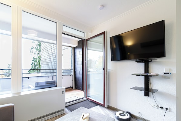 A modern room with a large TV mounted on the wall, a sliding glass door leading to an outdoor area, and a small table with a remote control.