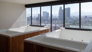 A modern bathroom with two large tubs, wooden cabinetry, and a city view through large windows. - Casa Bee walking distance to Reforma (Ciudad de México)