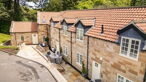 A row of stone buildings with red-tiled roofs, a patio with outdoor seating, and a small garden area. - East Hampton, Sandsend Retreats at Saltmoore - East Hampton (Whitby)