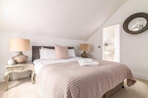 A bedroom with a bed, two bedside tables, a round mirror, and a view of the bathroom. - East Hampton, Sandsend Retreats at Saltmoore - East Hampton (Whitby)