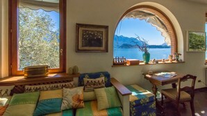 Une pièce chaleureuse avec une grande fenêtre donnant sur un lac, un canapé agrémenté de coussins à motifs, une table en bois et un tableau encadré accroché au mur.