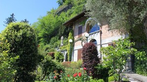 Un bâtiment traditionnel en pierre, doté d’un jardin et entouré d’une végétation luxuriante et d’arbres.