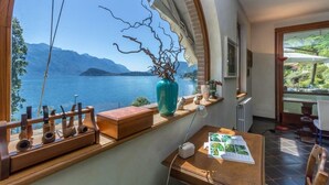 Une pièce dotée d’une grande fenêtre donnant sur un lac, d’un bureau en bois avec une lampe et d’un vase décoré de branches.