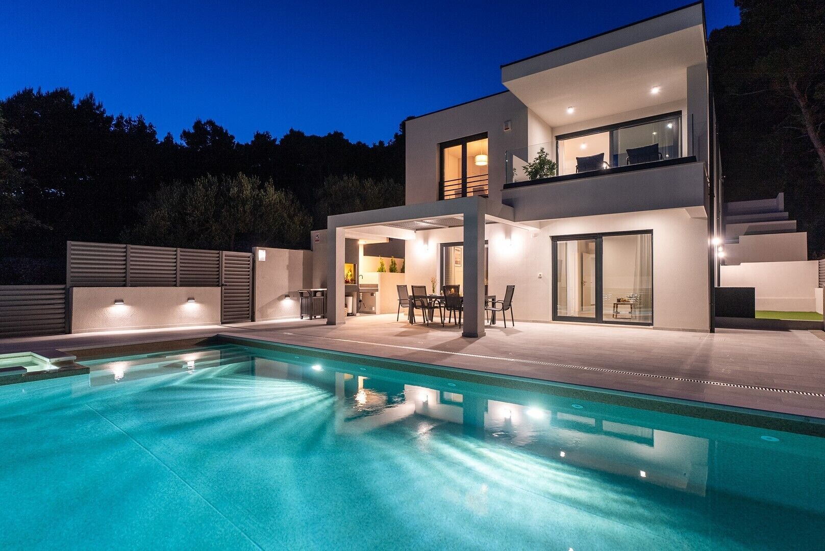 Una casa moderna de dos pisos con piscina, zona de estar exterior y un patio bien iluminado.