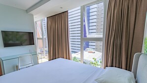 Una habitación de hotel con una cama grande, un televisor montado en la pared y vistas de la ciudad a través de amplias ventanas.