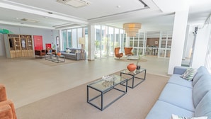 Un espacioso vestíbulo de hotel con diseño moderno, que incluye una zona de estar con sofás y sillones, una mesa de centro de vidrio y un amplio ventanal con vistas al exterior.