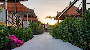 A pathway leading to traditional-style buildings with red-tiled roofs, surrounded by lush greenery and flowering plants. - Island Retreat Cottage (Lembongan Island)