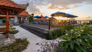 A resort with a traditional tiled roof, outdoor seating with umbrellas, and a garden area with steps leading to a pool. - Island Retreat Cottage (Lembongan Island)