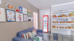 Una sala de estar con un sofá azul, un refrigerador Coca-Cola rojo y varias obras de arte enmarcadas en la pared.