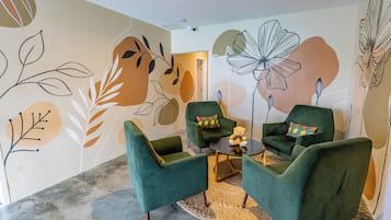 Ein modernes Wohnzimmer mit grünen Sesseln, einem kleinen Couchtisch und abstrakter Wandkunst.