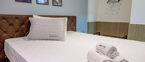 A neatly made bed with a pillow, a wall with framed pictures, and rolled towels on the bed.