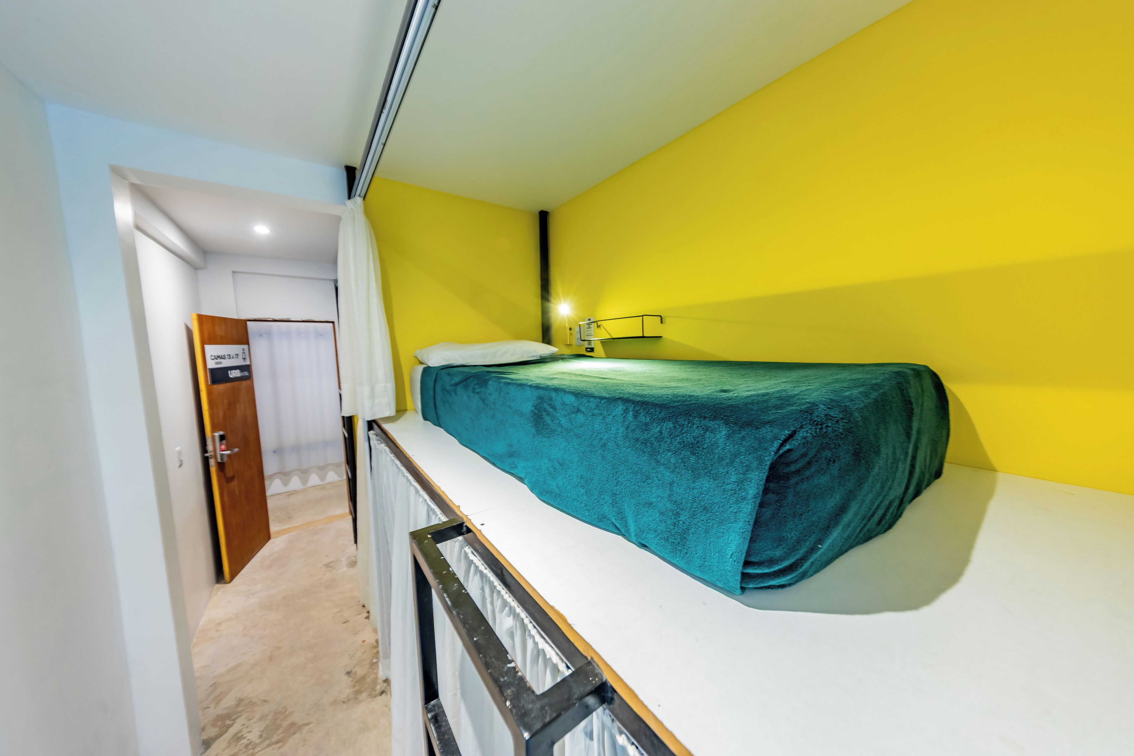 A small, narrow room with a bunk bed, a door leading to another room, and a wall-mounted light fixture.